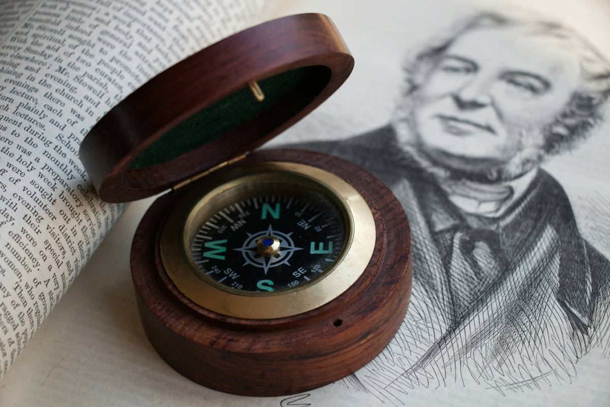 A vintage brass compass resting on a wooden bookshelf beside a floor plan sketch and measuring tape — compasses at home